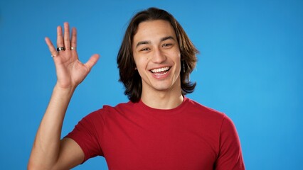 Portrait of happy smiling Hispanic Latino gender fluid young man 20s having a video chat, as seen from the point of view of a computer screen. Isolated on blue background.