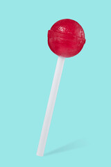 Close-up of a red lollipop in the shape of a ball on a stick, isolated on a beautiful turquoise...