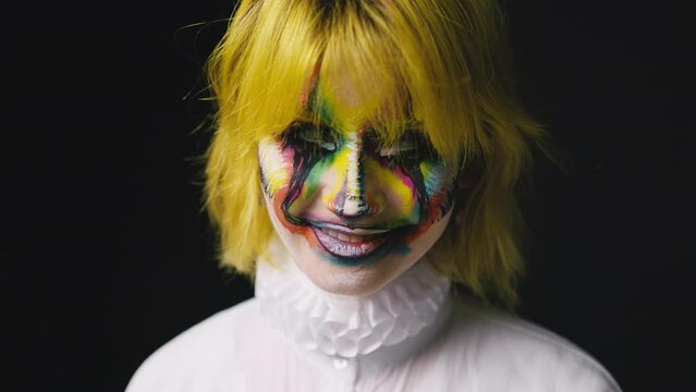 Close up shot of young woman with yellow hair and clown art face, haloween scarry face on black background