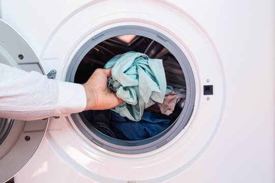 Closeup of a hand of a man putting dirty cloth into the washing machine