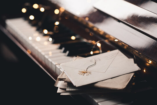 Paper snail mail letters in envelope on piano keys with dry flowers over glow Christmas lights close up. Romantic lifestyle. Valentines Day.