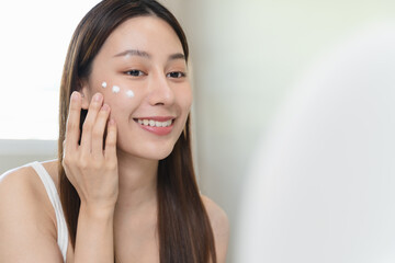 Asian young woman applying cream to her face in routine self care.