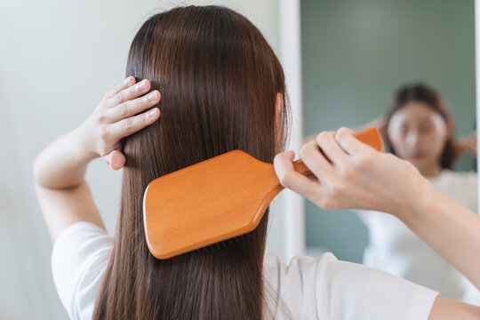 Happy asian woman brushing hair by wooden comb in the morning.