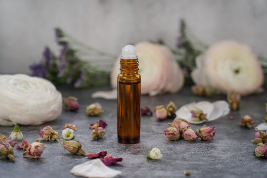     Under eye roll on in amber glass bottle on grey background with flowers. Rose eye serum. Cosmetics packaging.   