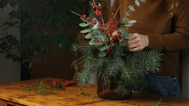 Woman creates Christmas flower bouquet. Winter holiday home decor.