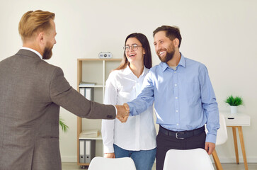 Happy couple shaking hands with real estate agent. Joyful, smiling young man and woman meeting with...