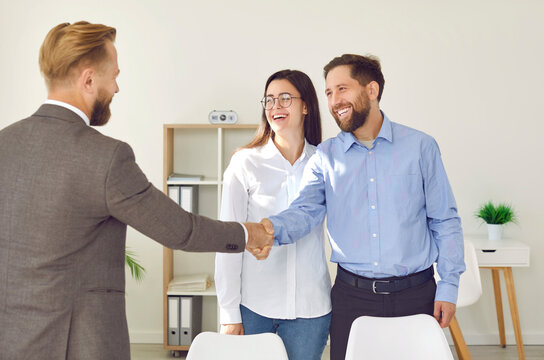 Happy couple shaking hands with real estate agent. Joyful, smiling young man and woman meeting with professional realtor, making deal, exchanging handshakes and thanking him for service