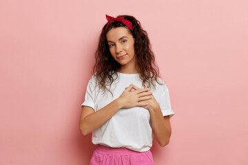 Young woman puts hands on the chest, isolated over pink background