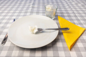 Laid table, with white plates and glass containing plastic waste. Plastic in the environment and microplastics in food. 

