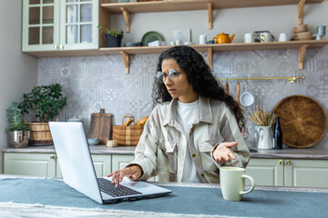 Young hispanic female freelancer in glasses can't work on laptop at home. The lights are off, the...