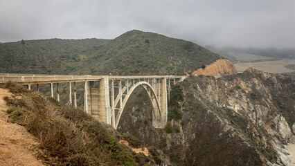 The Bixby Bridge in the Big Sur coastal area with steep cliffs nearby in the US state of California on a cloudy foggy day.