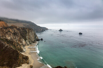 Obraz premium The Big Sur coastal area with crags and cliffs in the US state of California on a cloudy foggy day, photo taken near the Bixby Bridge, USA