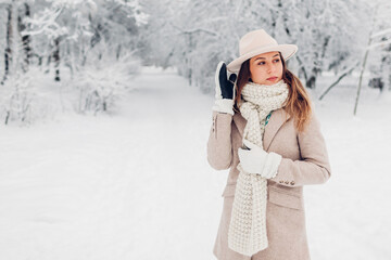 Fototapeta na wymiar Winter female fashion. Portrait of stylish young woman in snowy winter park wearing white and beige warm clothes