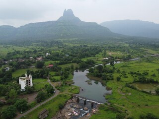 Aerial view of the river and greenery before the silhouettes of Malang Gad on the mountains © Harshal Khutarkar/Wirestock Creators