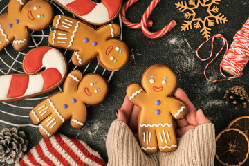 Woman hands hold decorated gingerbread man with white icing. Homemade traditional festive Christmas cookies. Flat lay. Winter holidays background. Merry Christmas and Happy New Year