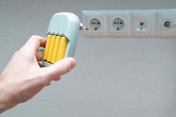 Charger and Batteries in man`s hand. Male hand holding charger with yellow AA batteries, on white...