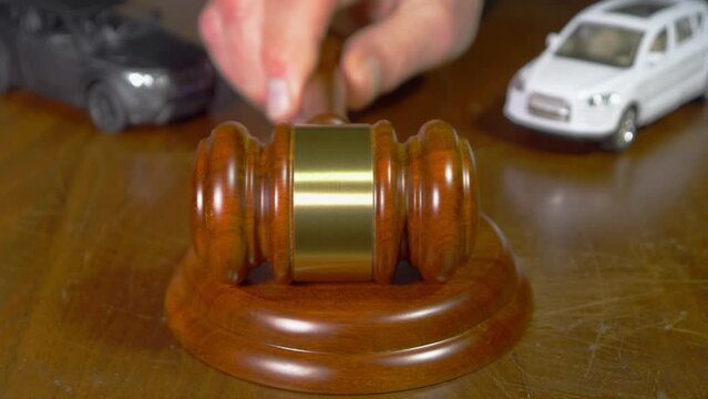 Car auction concept: Closeup of a man&rsquo;s hand striking a traditional wooden gavel against a matching wood block, with two defocused model cars in the background.