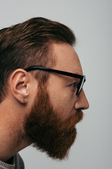 Obraz premium Side view of bearded man in eyeglasses looking away isolated on grey.