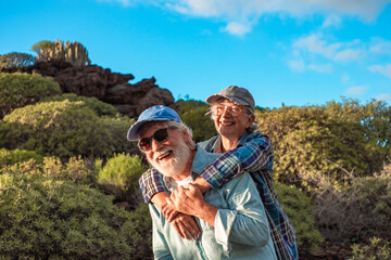 Happy caucasian senior couple enjoying travel and nature in mountain range. Man carries piggyback...