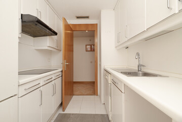 Fototapeta na wymiar Kitchen with white furniture with drawers, floors, walls and ceilings of the same color and pear-colored wooden access door