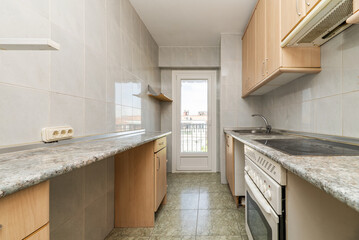 Kitchen of a house with furniture on both walls with light green wooden countertop, aluminum door leading to a terrace and wooden furniture