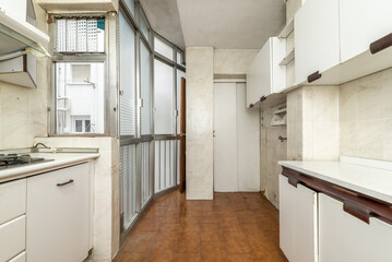 Old kitchen of a house with white furniture, aluminum partition and translucent glass and brown stoneware floors