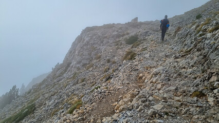 Man trekking on mystical foggy hiking trail leading to Mount Olympus (Mytikas, Skala, Stefani) in...