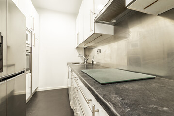 Kitchen with white cabinets with stainless steel handles, on gray and stainless steel veneered wall and column with appliances