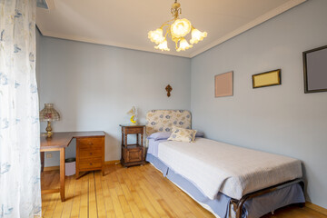 Youth bedroom with metal bed and fabric headboard, wooden slatted floor and antique wooden furniture