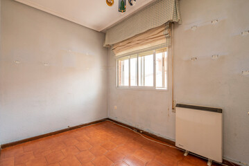 Empty bedroom with dirty walls, orange stoneware floors and electric heat accumulator