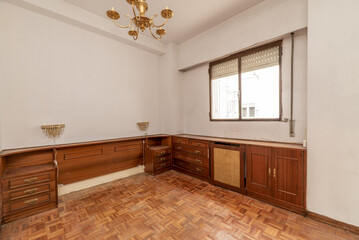 Empty bedroom with plain white walls, wooden bed headboard with drawers and gold bedside lamps
