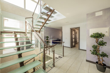 Interior of a detached house staircase with stoneware floors, a metal design staircase with tempered glass steps