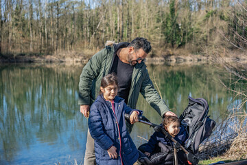 Father with stroller and two children walking along the Aare river in springtime.