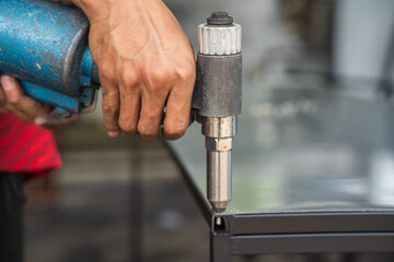 An industrial worker uses an air pop rivet gun to fasten workpieces with aluminum nails.