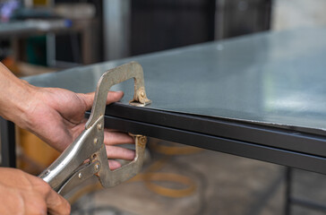 A factory worker is using C-clamp pliers to hold steel and galvanized sheets.