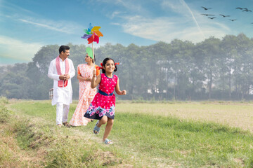 Happy parents with cute little girl running carefree and having fun with colorful pin wheel.