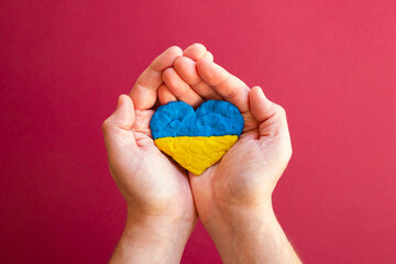 Flag of Ukraine. Heart shape of blue and yellow plasticine modeling clay in male man hands on red background. Ukrainian flag concept, love. Top view