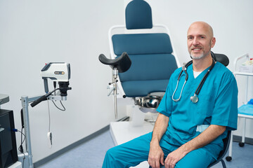 Doctor in medical uniform is next to gynecological examination chair - obrazy, fototapety, plakaty