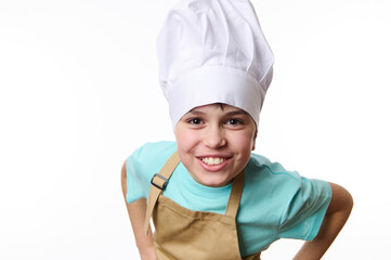 Close-up overjoyed happy pre-adolescent child- chef pastry, cook, baker confectioner wearing chef hat and beige apron, smiling a cheerful toothy smile looking at camera, isolated on white background