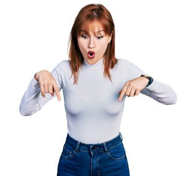 Redhead young woman wearing casual turtleneck sweater pointing down with fingers showing advertisement, surprised face and open mouth