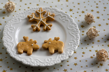 Fototapeta na wymiar Painted traditional Christmas gingerbreads arranged on white plate, tablecloth with golden stars, snowflake and reindeer shapes