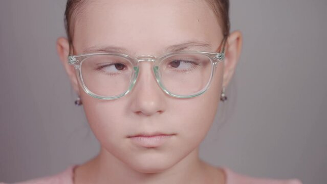 Funny close-up of serious teen girl with glasses strabismus squints her eyes looking at camera.