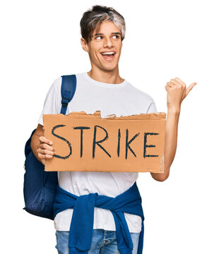 Young hispanic man holding strike banner cardboard pointing thumb up to the side smiling happy with open mouth