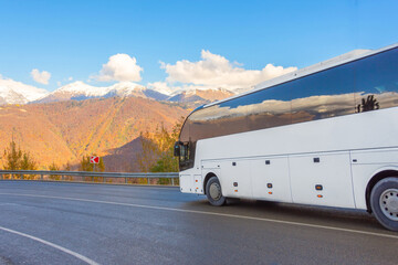 White tourist bus rides at a turn along a serpentine road against the backdrop of snow-capped mountain peaks.