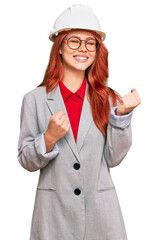 Young redhead woman wearing architect hardhat excited for success with arms raised and eyes closed celebrating victory smiling. winner concept.