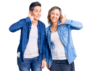 Couple of women wearing casual clothes smiling doing phone gesture with hand and fingers like talking on the telephone. communicating concepts.