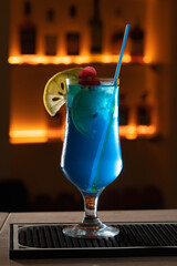 Closeup glass of Blue Lagoon Cocktail decorated with lime at bar counter background.