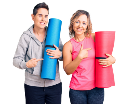 Couple of women holding yoga mat smiling happy pointing with hand and finger