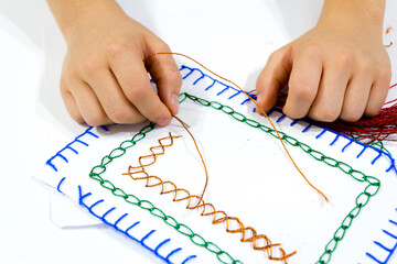 The closeup of hands sewing a colorful card during school activities. An ideal DIY stitch with...