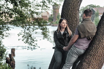 Happy young couple holding hands, woman and man together spending summertime outdoors. Caucasian couple enjoy leisure activity in park with lake. Concept of good family relationship. Copy text space